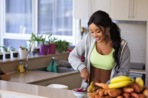 A woman in her kitchen slicing a pear next to a bowl of fruits and vegetables