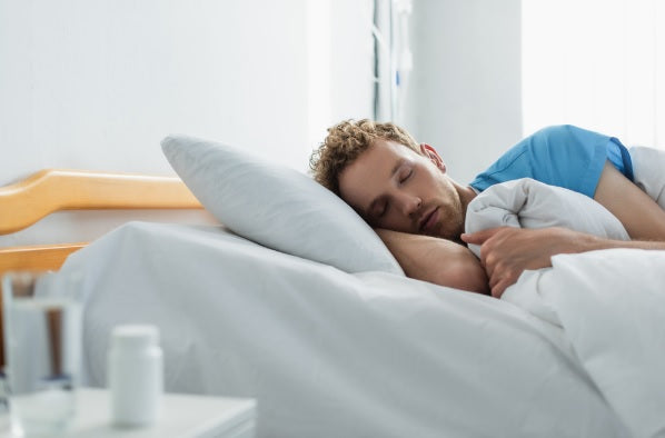 Curly patient sleeping in hospital bed near blurred bottle with medication and glass of water 